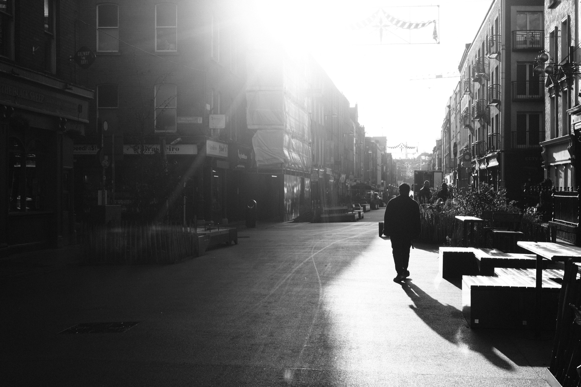 A person walking down an empty street into the morning sun.